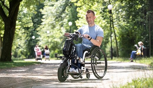 Mann im Rollstuhl mit elektrischem Zusatzantrieb im Park als Beispiel für aktive Mobilität bei Saniplus Baunatal